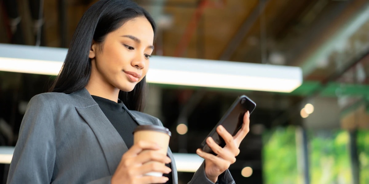 Woman holding phone and coffee in an office