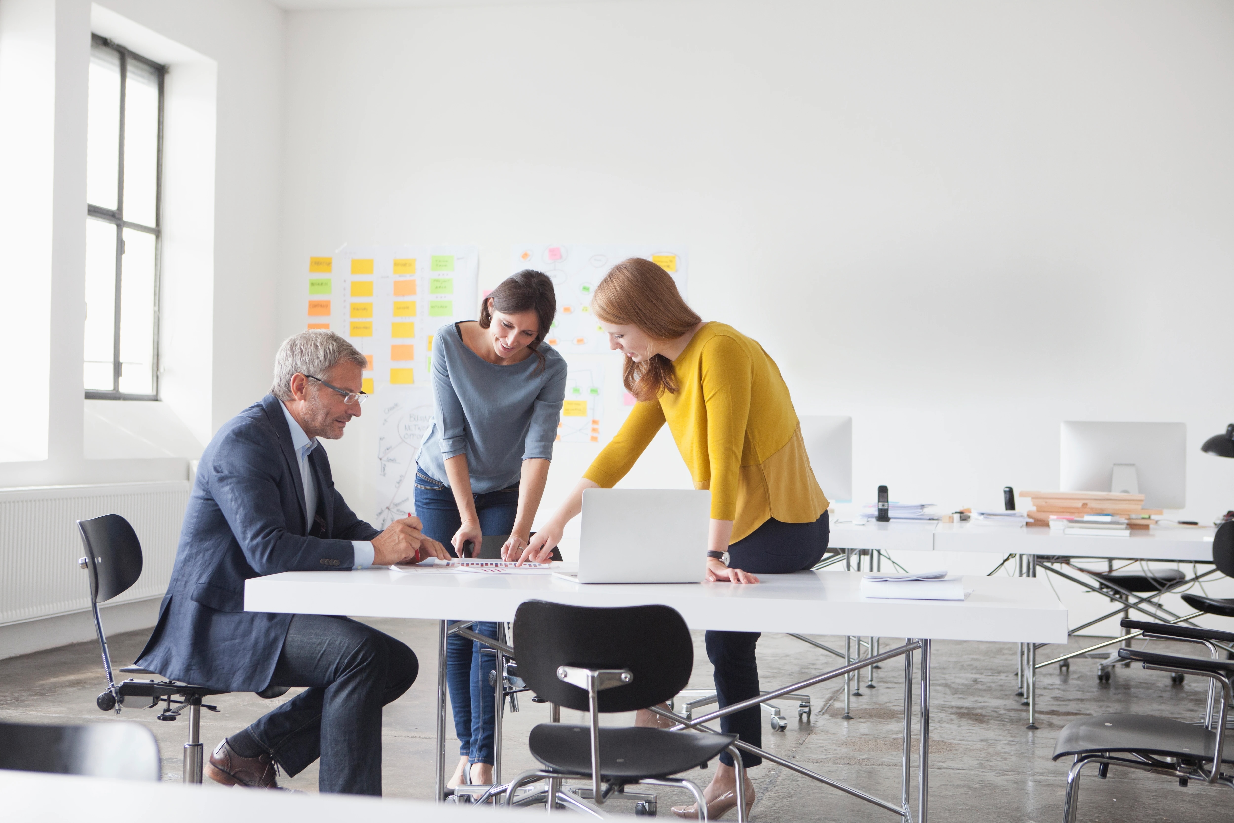 Three people standing around a laptop in an office