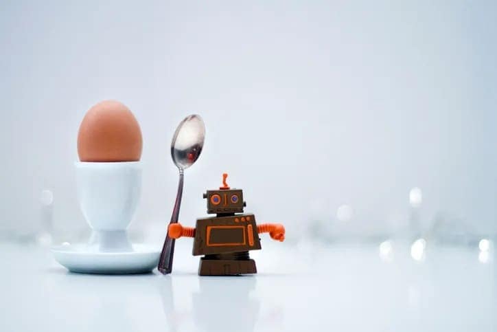 Small robot holding a spoon next to an egg in an egg cup