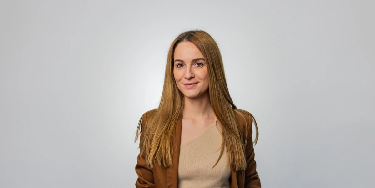 Red-haired woman in brown blazer against plain grey background