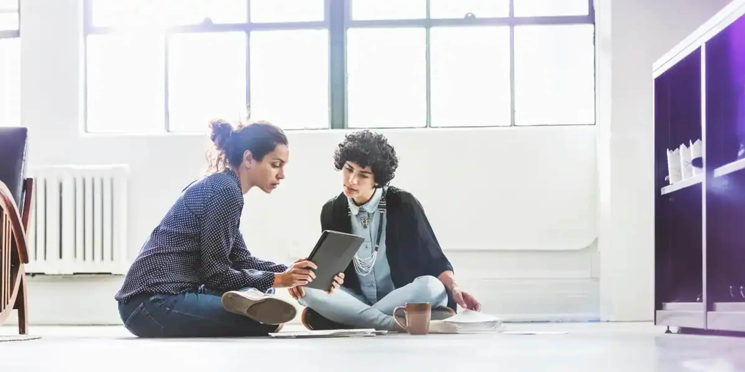 Two women sitting on the floor looking at a tablet