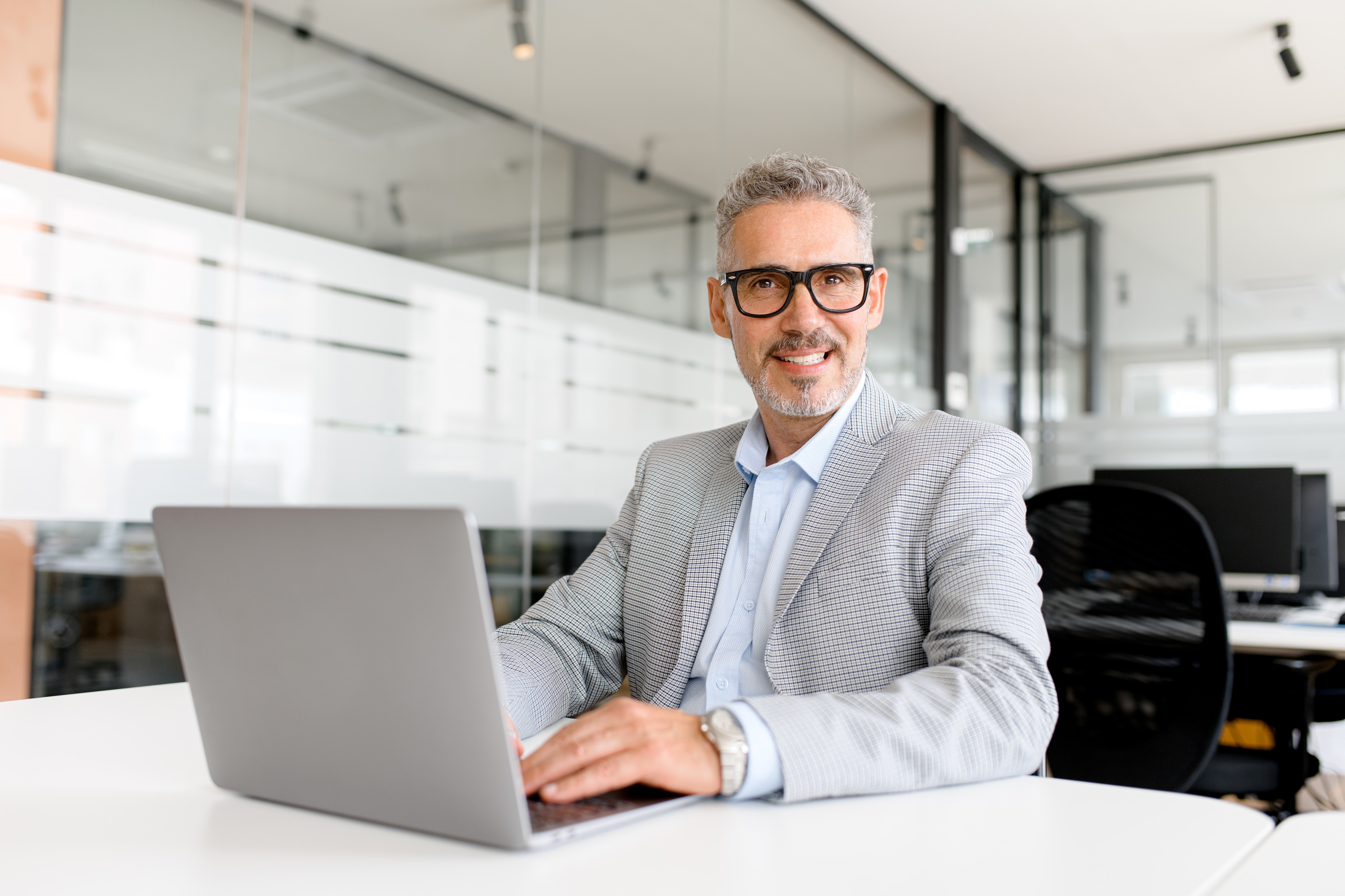 Man smiles at camera while working on laptop
