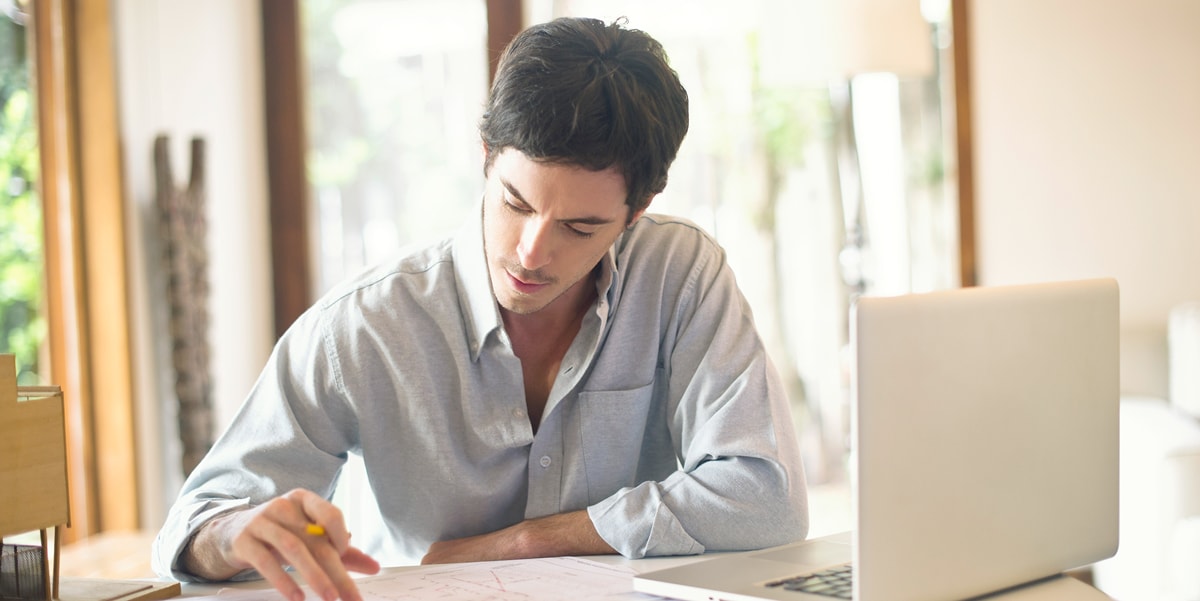 Man reading physical documents with a laptop nearby