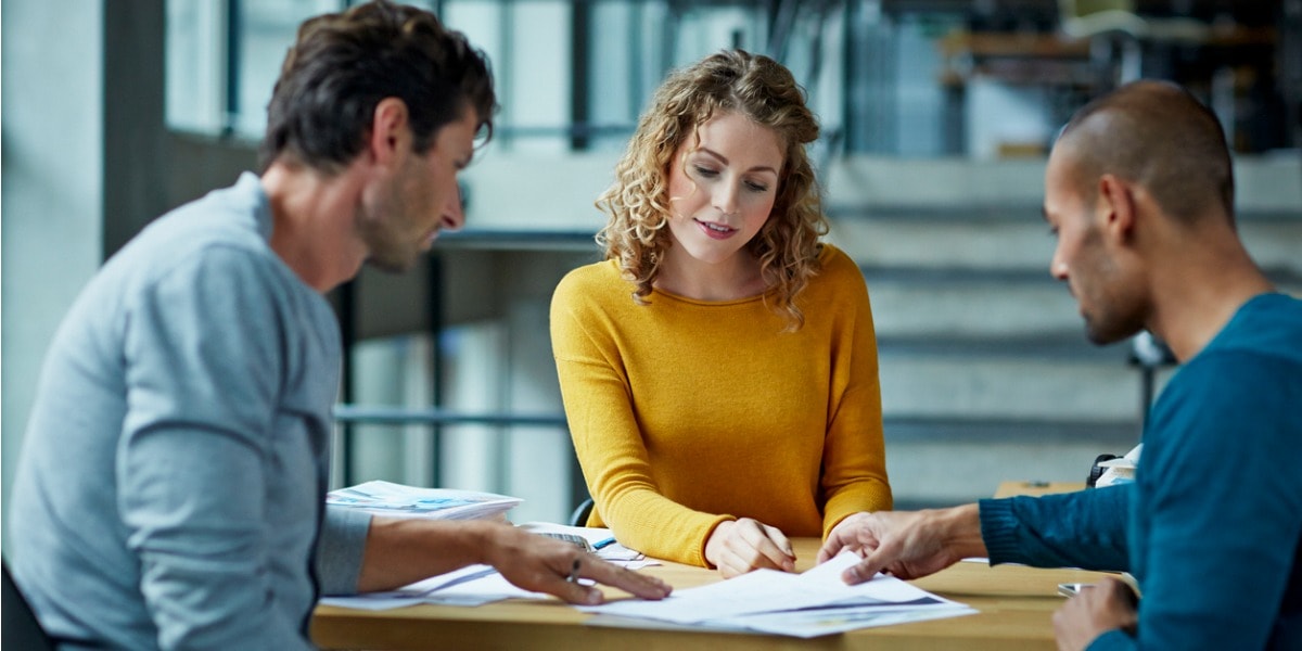 three people having a discussion and working on a laptop in an office