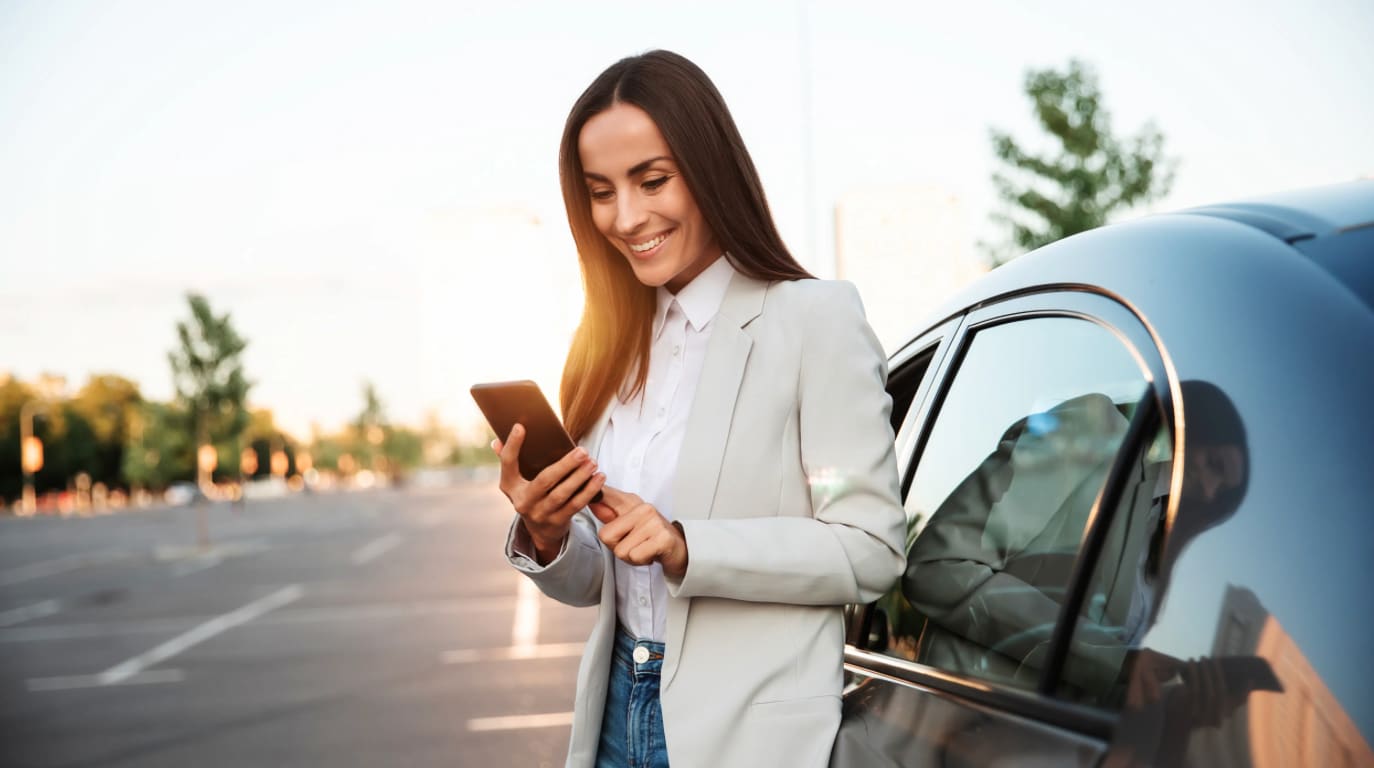 female business traveler standing outside of car looking at phone